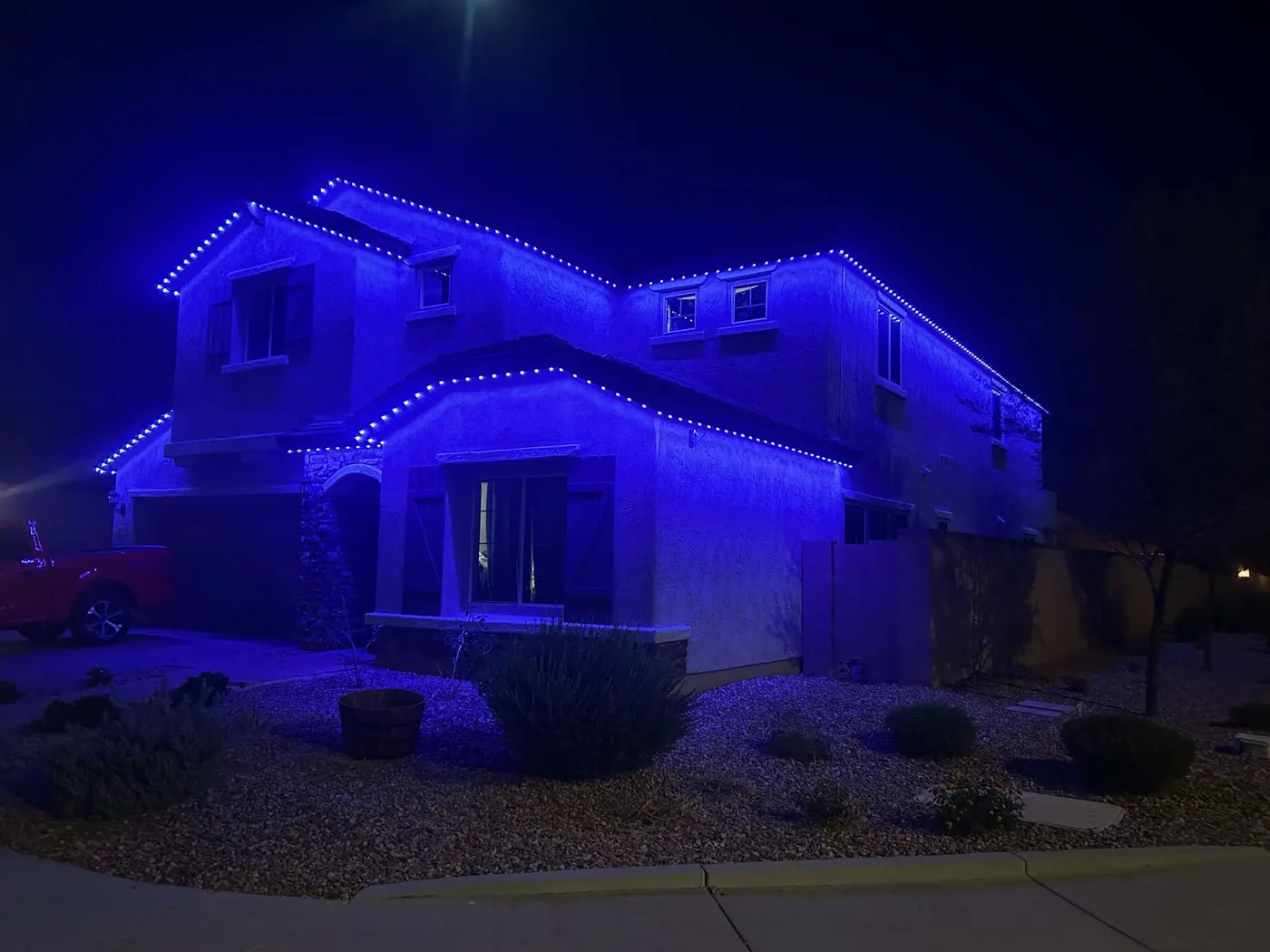 Two story stucco home with blue permanent lighting along every roofline and gable