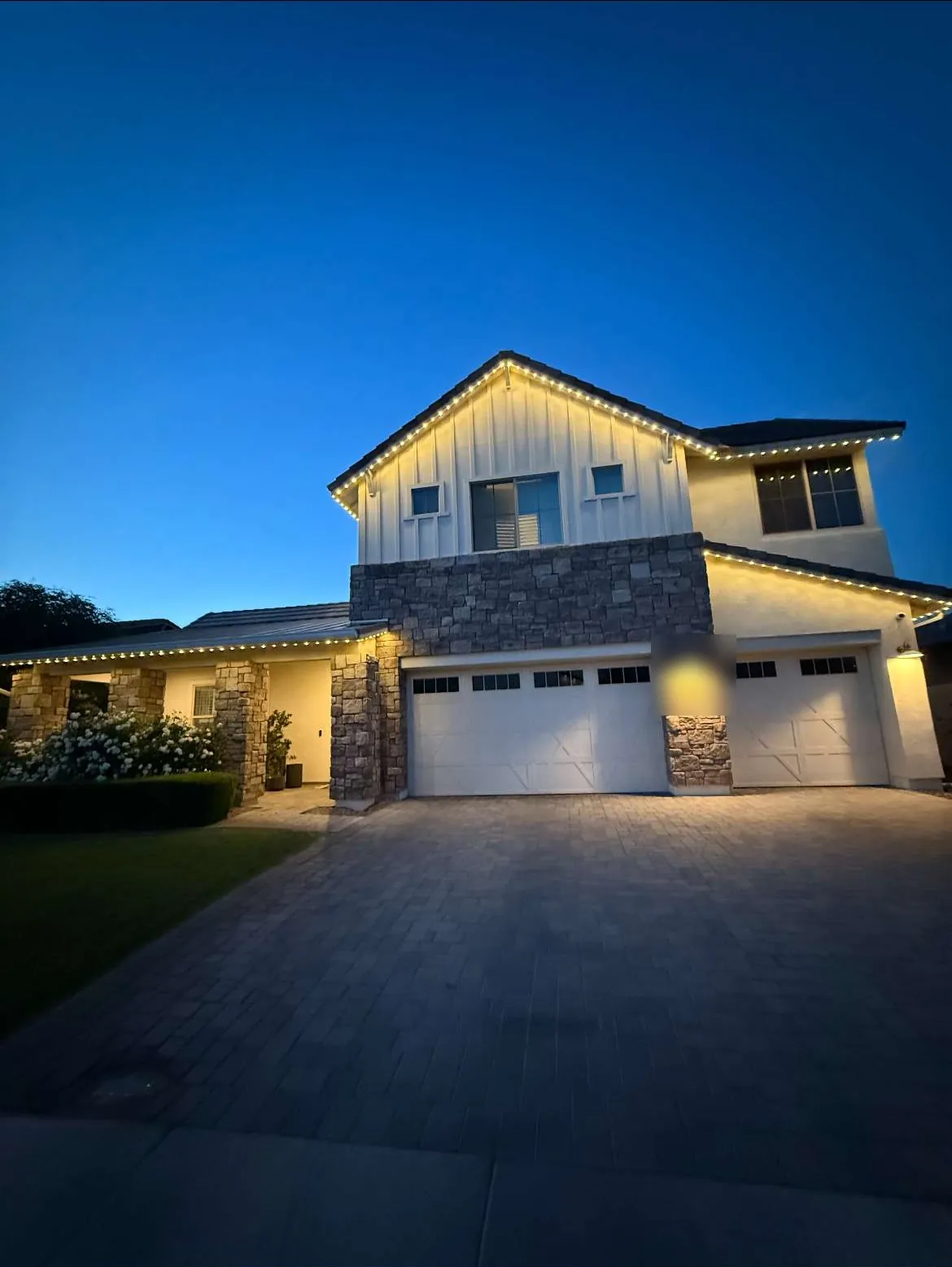 Modern farmhouse at blue hour with warm white permanent lighting along the gables and roofline